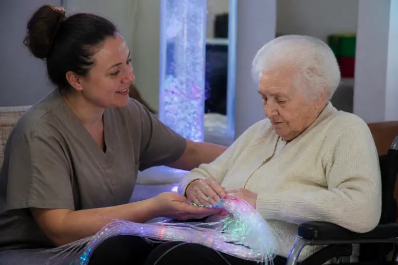 Un soignant accompagne un résident lors d'une séance sensorielle snoezelen ehpad dans une pièce calme.