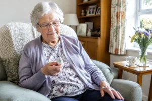 Une personne âgée tenant un boîtier de téléassistance sans abonnement dans son salon lumineux
