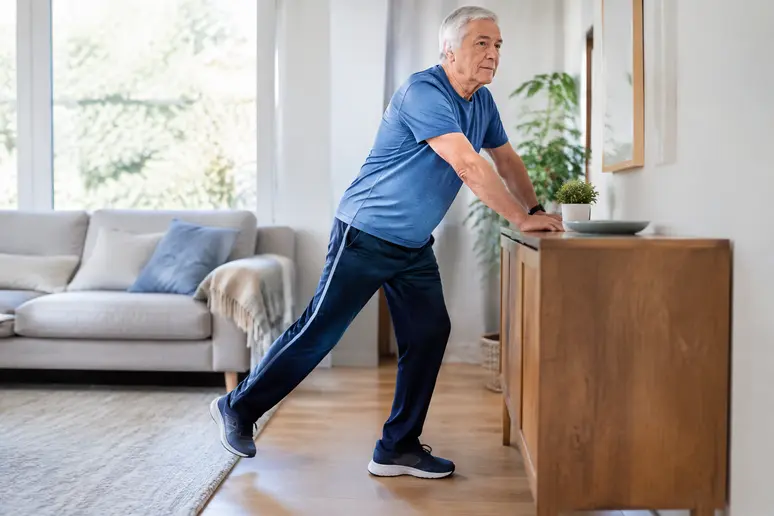 Un senior en tenue de sport réalise des mouvements de renforcement musculaire senior dans son salon lumineux