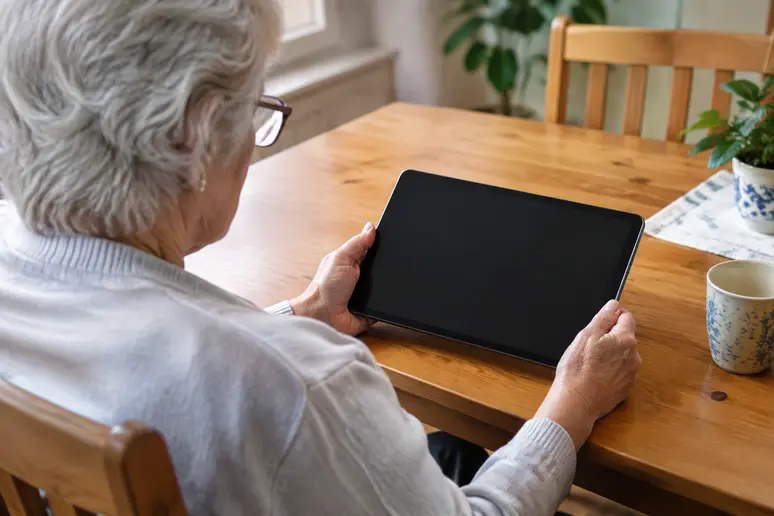 Une personne âgée utilise une tablette senior sans abonnement installée confortablement à son domicile